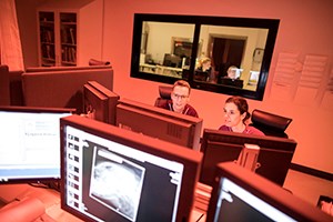 Två personer i rött rum med flera datorskärmar. Foto